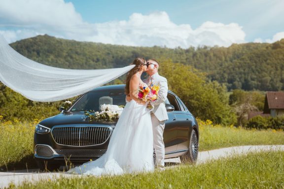 Brautpaar küsst sich vor dem Hochzeitsauto während eines romantischen Brautpaarshootings nähe Stuttgart.